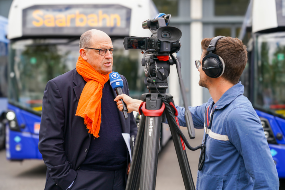 Geschäftsführer Karsten Nagel im Interview Karsten Nagel führt ein Interview mit dem SR. Im Hintergrund ist ein neuer Wasserstoffbus zu sehen .